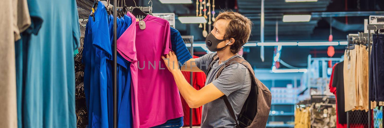 Man in a clothing store in a medical mask because of a coronovirus. Quarantine is over, now you can go to the clothing store BANNER, LONG FORMAT by galitskaya