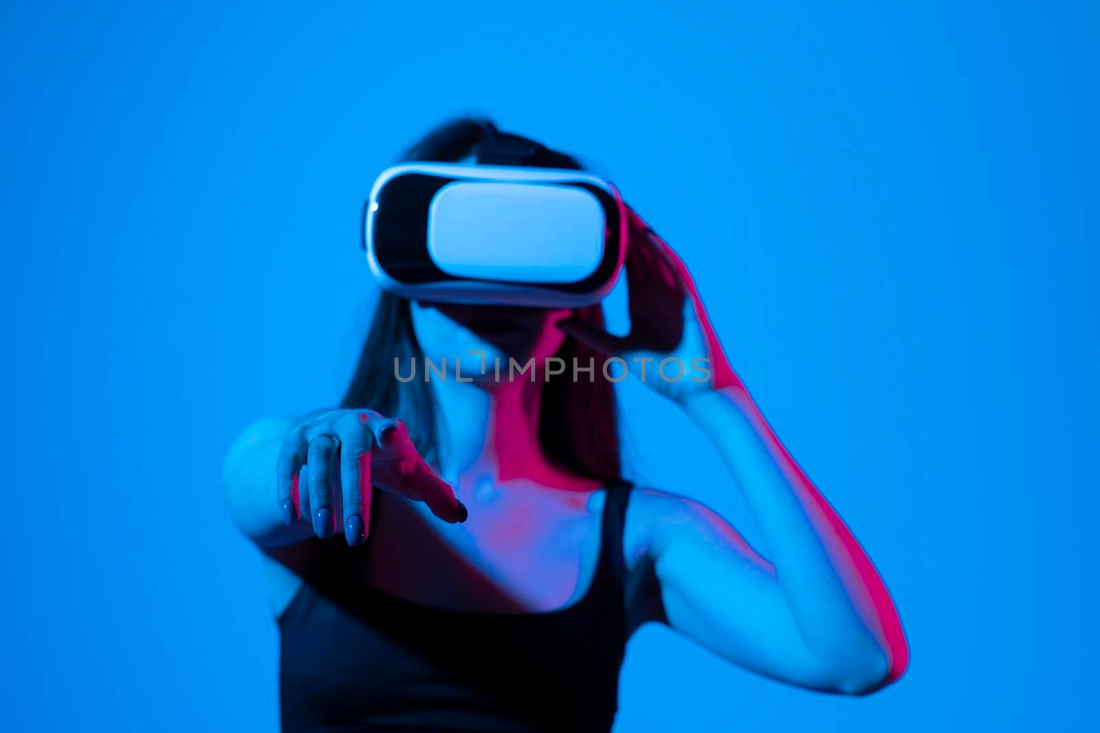 Cheerful girl with hands up wearing the virtual reality goggles and playing a games in neon light. Future technology concept. Metaverse