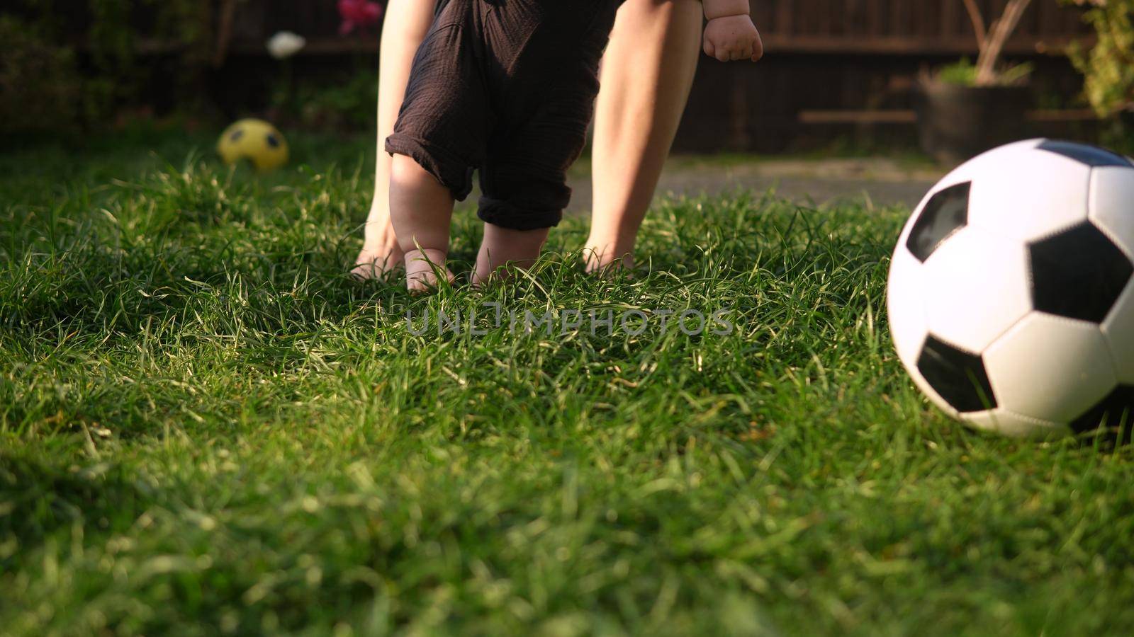 Baby Takes First Steps On Green Grass. Happy Young Cheerful Mother With Adorable Infant Baby Playing Outdoors With Love In Backyard Garden. Little Children With Parents. Family, Nature Ecology Concept.