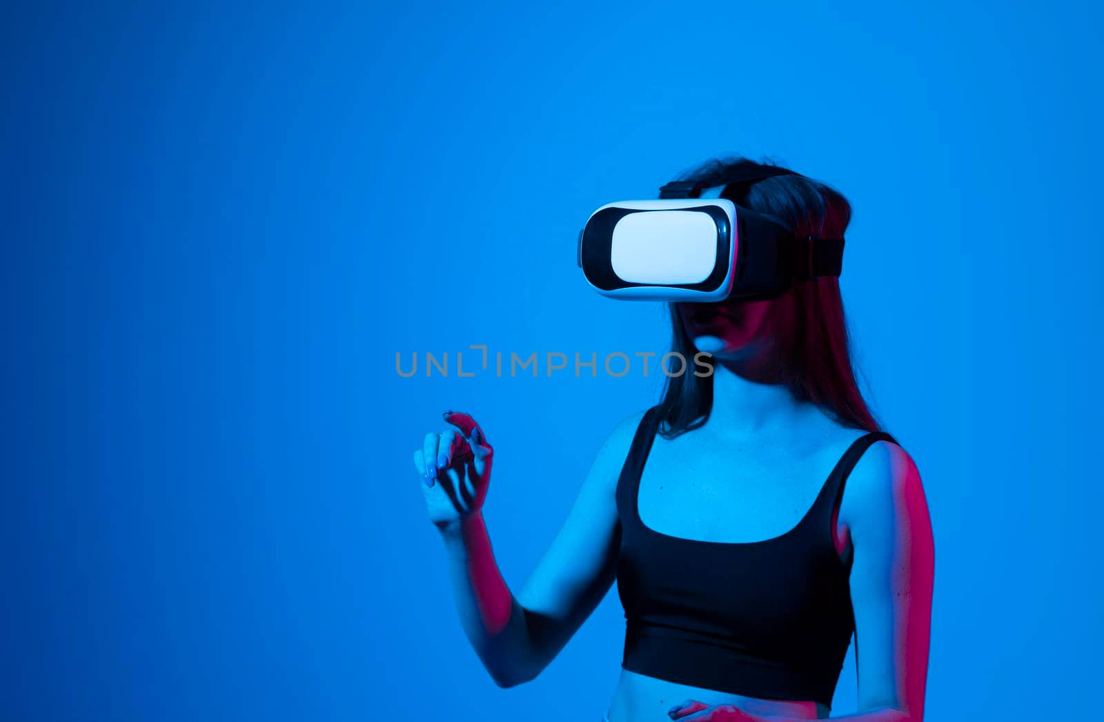 Portrait of young woman playing in VR-glasses in neon light on blue background. Concept modern gadgets and technologies. Future technology concept. Virtual reality gaming. by vovsht