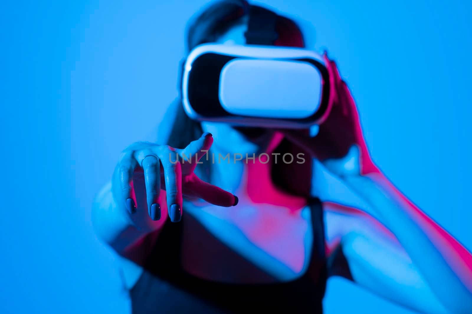 Young girl playing game using VR glasses, enjoying virtual reality headset while gaming with a friends in metaverse in neon light. by vovsht