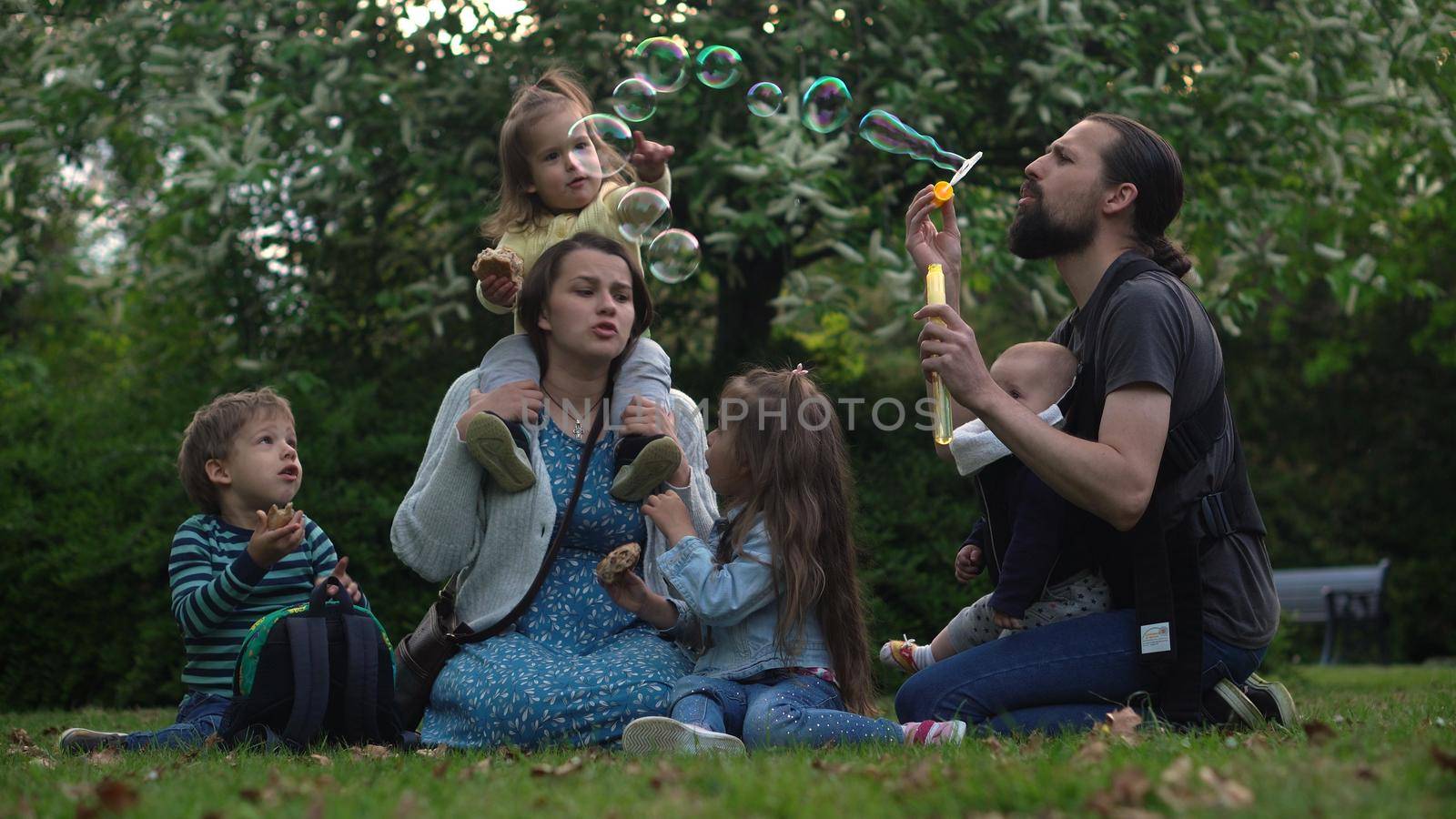 Happy family mother Father Three four Baby little siblings kids have fun blowing bubbles enjoying summer holidays in garden park. Smiling parents children spending leisure time together evening sunset by mytrykau