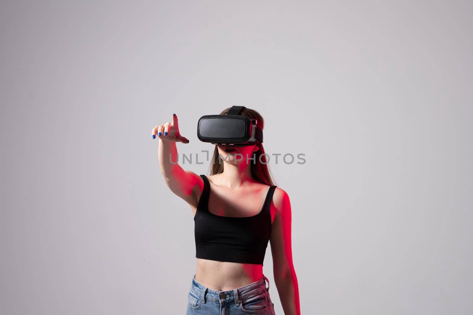 Young woman working in VR goggles on a grey background. Modern architect using virtual reality glasses at workplace. Designer working in augmented reality vr studio