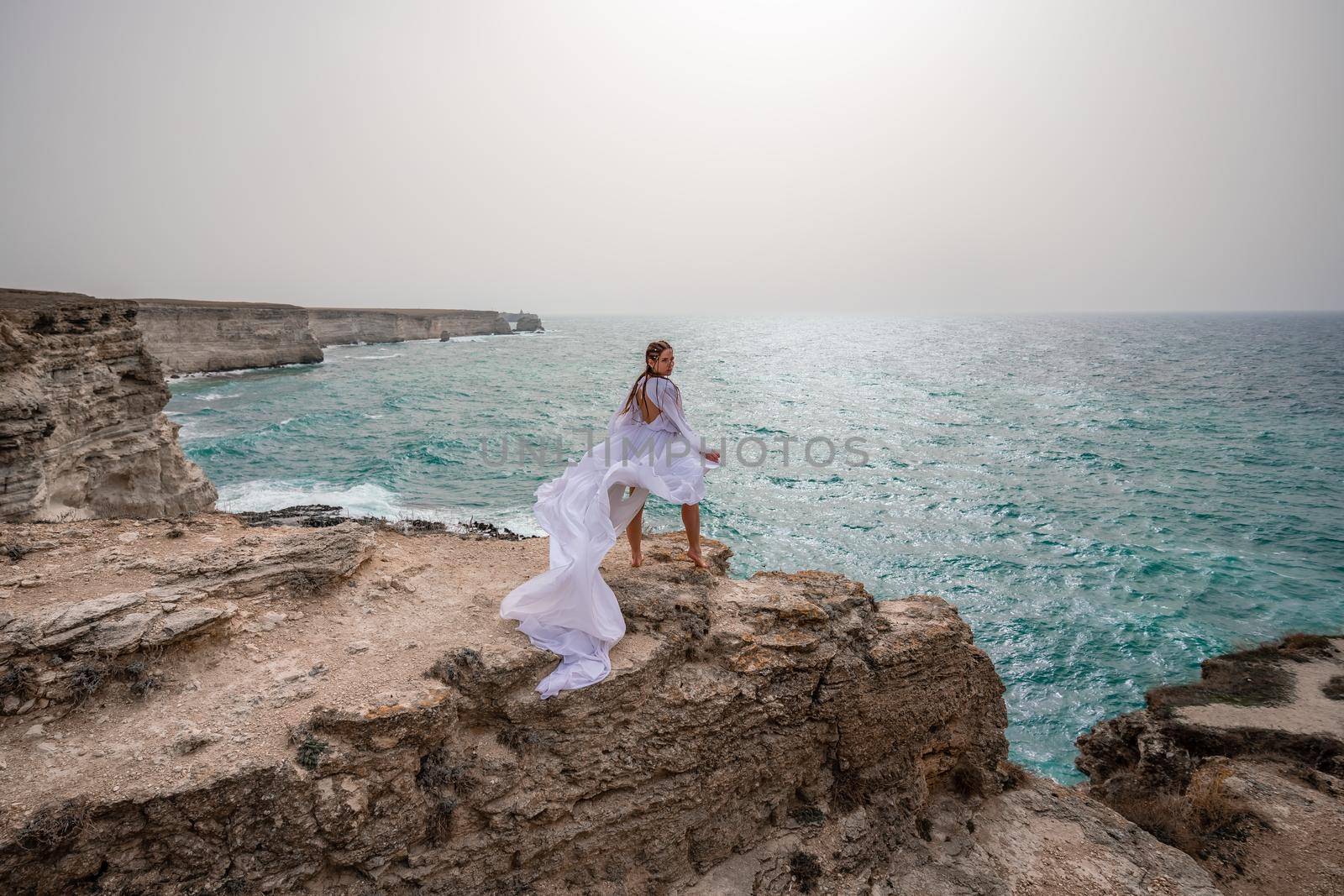 Happy freedom woman on the beach enjoying and posing in white dress over the sea. View of a girl in a fluttering white dress in the wind. Holidays, holidays at sea. by Matiunina
