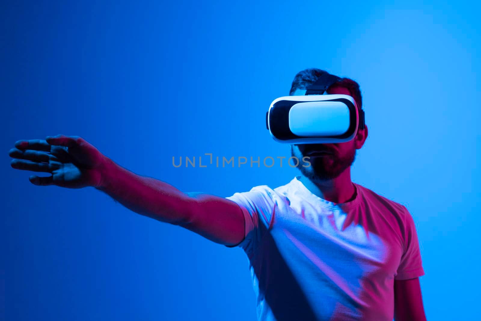 Young bearded man in virtual reality helmet plays online game in metaverse. Game simulates behavior in fictional world, gadgets and virtual reality addiction. Future technology concept