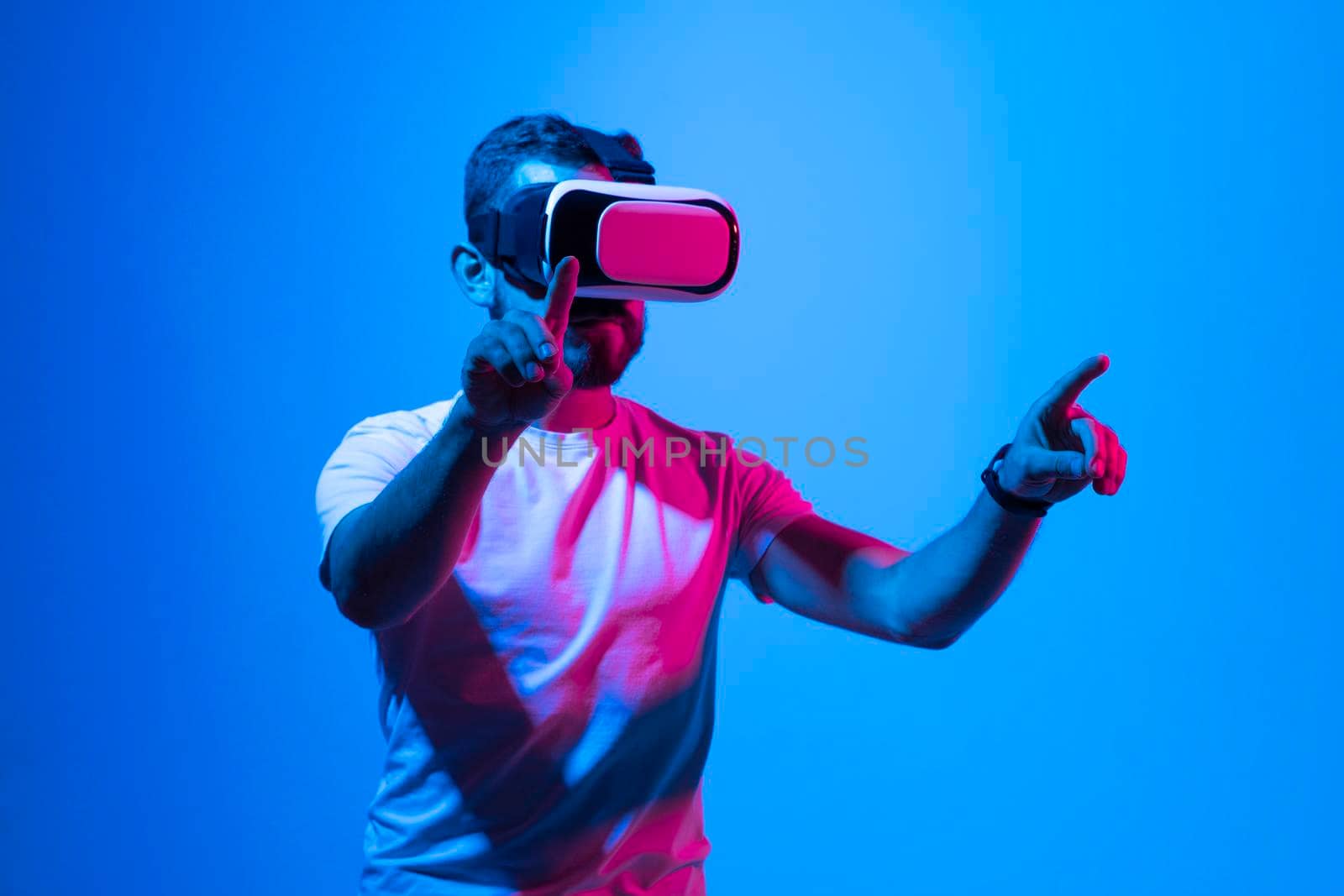 Bearded man playing VR video game in metaverse with virtual reality goggles and trying to touch something. Future technology concept. by vovsht