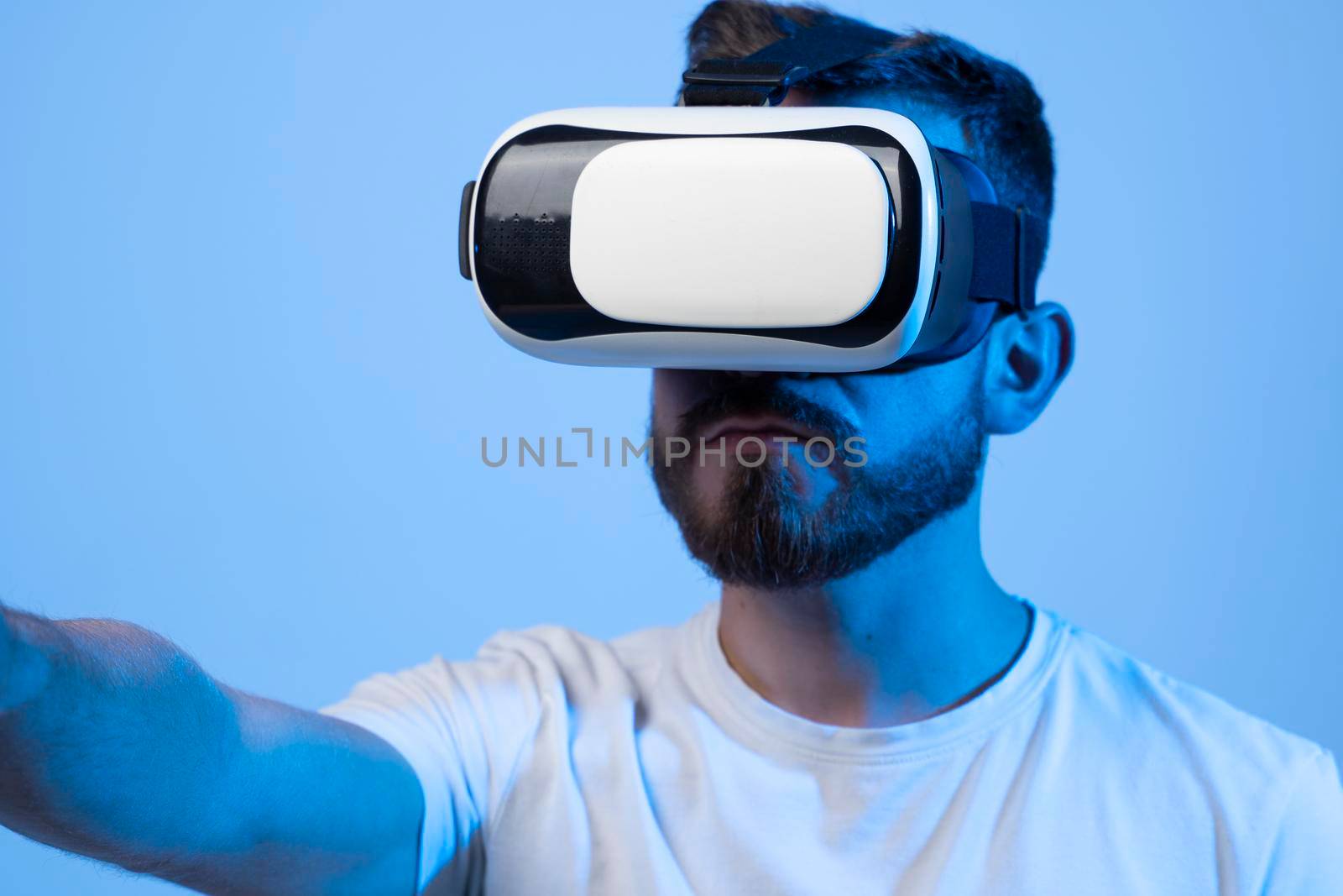 Young man using VR headset helmet to play simulation game. Watching virtual reality 3d video. Bearded man in VR goggles looking around. by vovsht