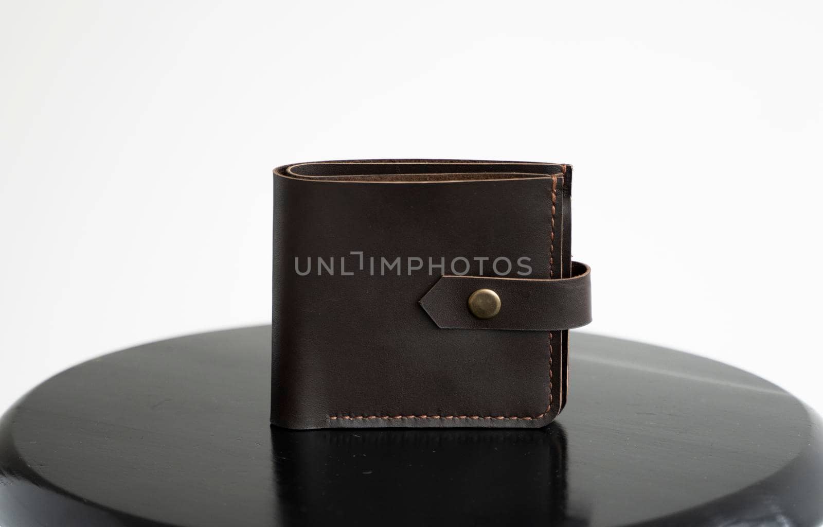 Man's black handmade genuine leather wallet for banknotes and credit cards on a black surface with white background. Style, retro, fashion, vintage and elegance