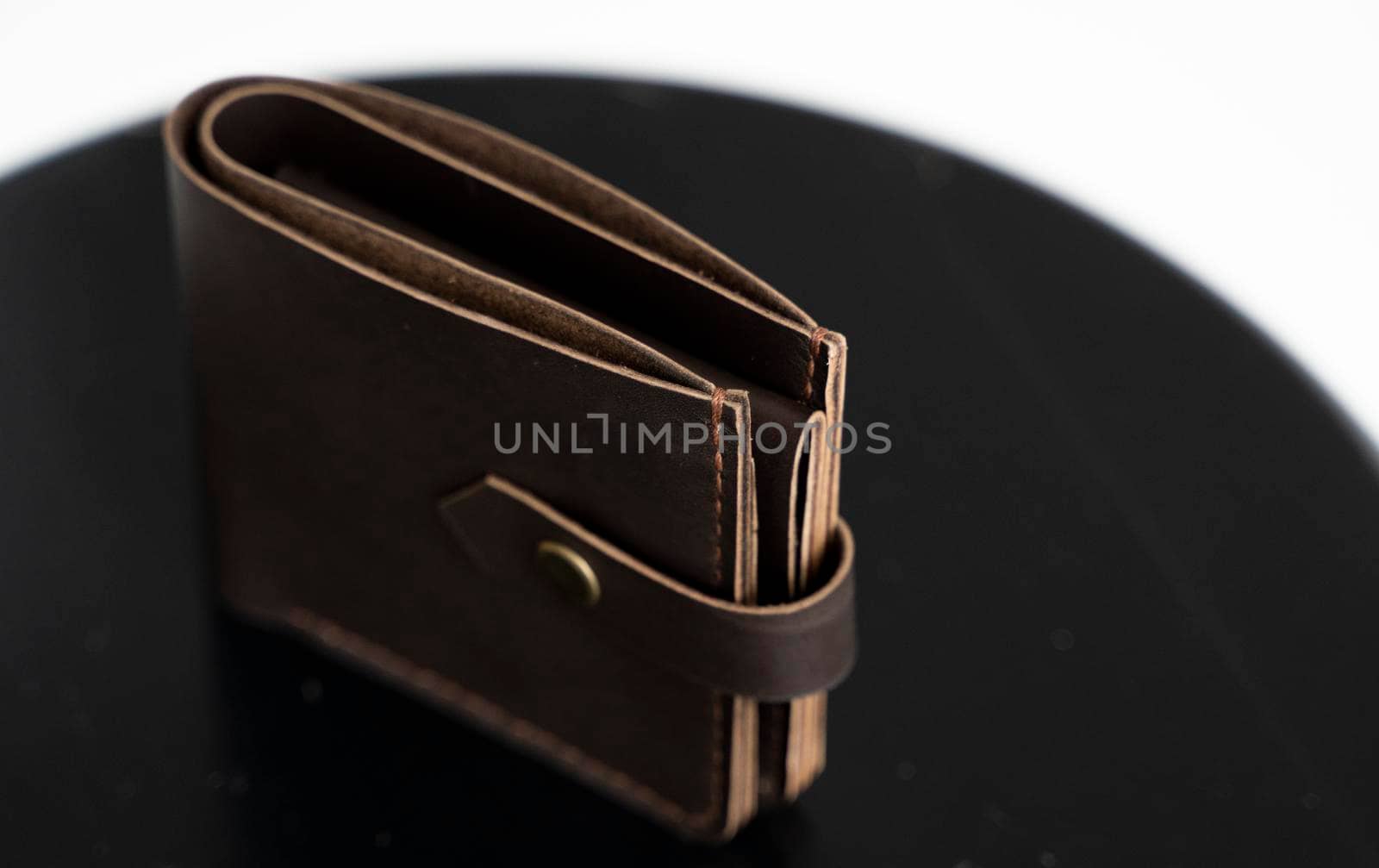 Man's black handmade genuine leather wallet for banknotes and credit cards on a black surface with white background. Style, retro, fashion, vintage and elegance