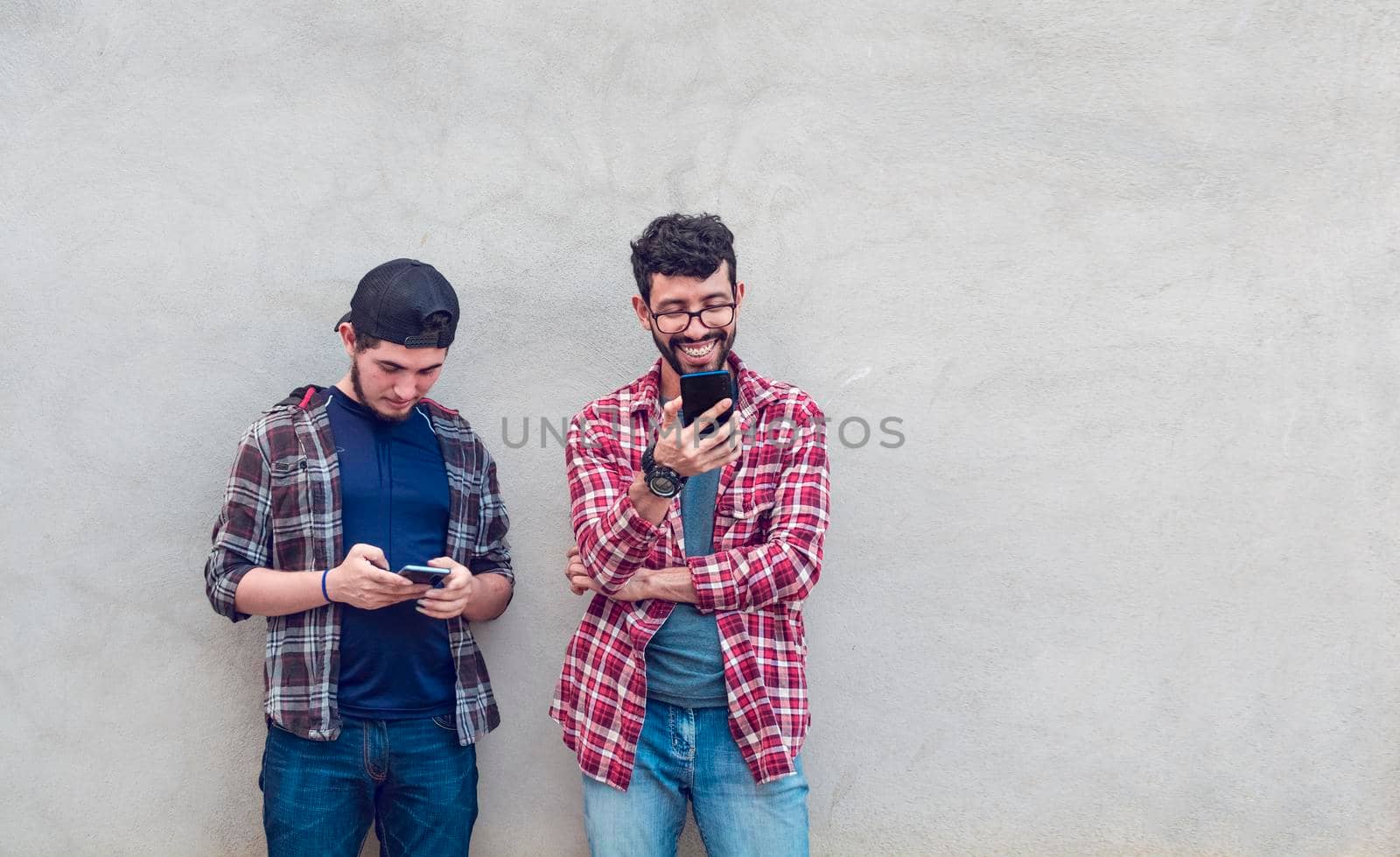 Smiling guys checking their cellphones, Smiling handsome young men checking their cellphones, Two guys enjoying their cellphone by isaiphoto