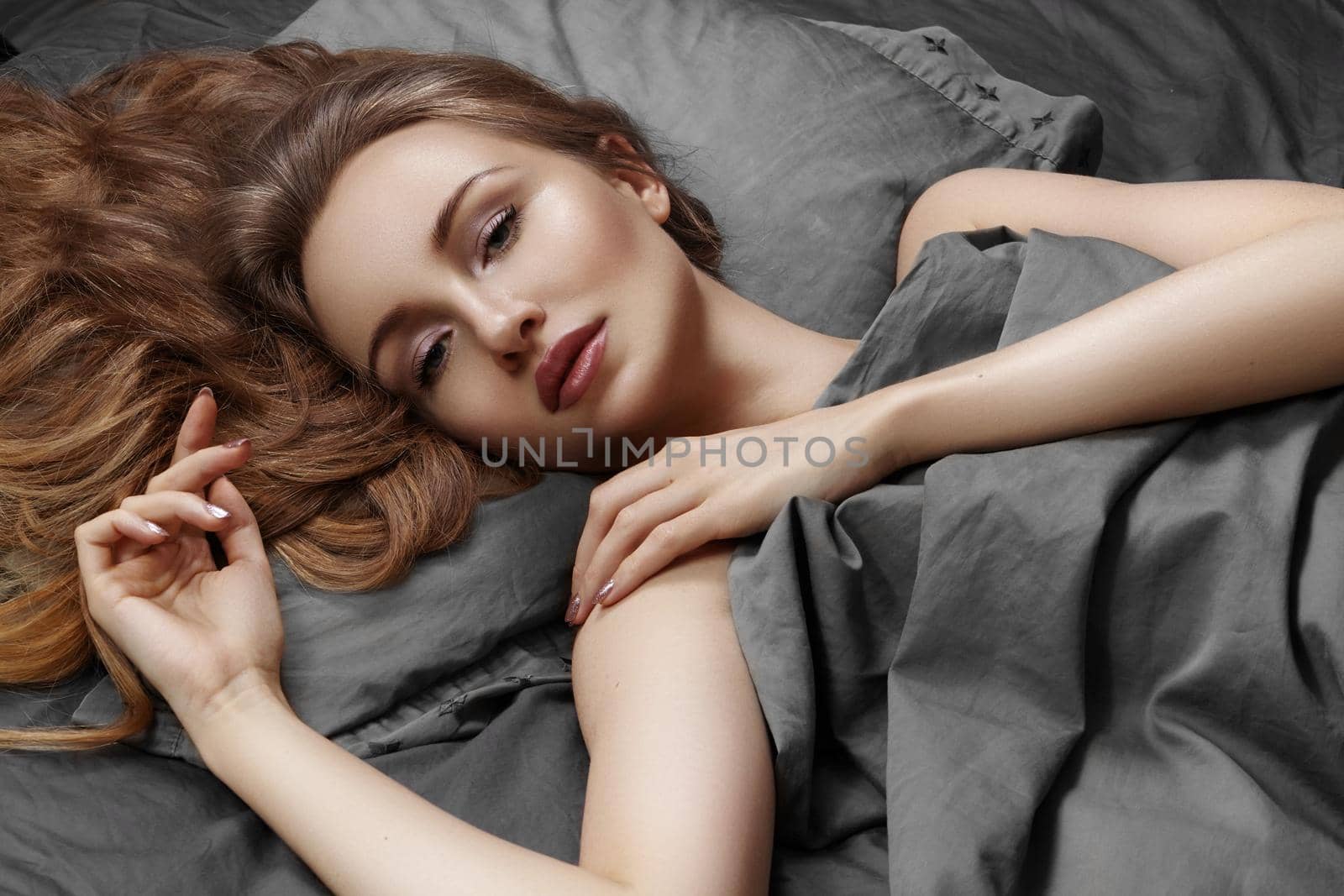 Beautiful Woman Sleeping while lying in Bed with Comfort. Sweet dreams. Sexy model with long curly hair relaxing on grey sheets.