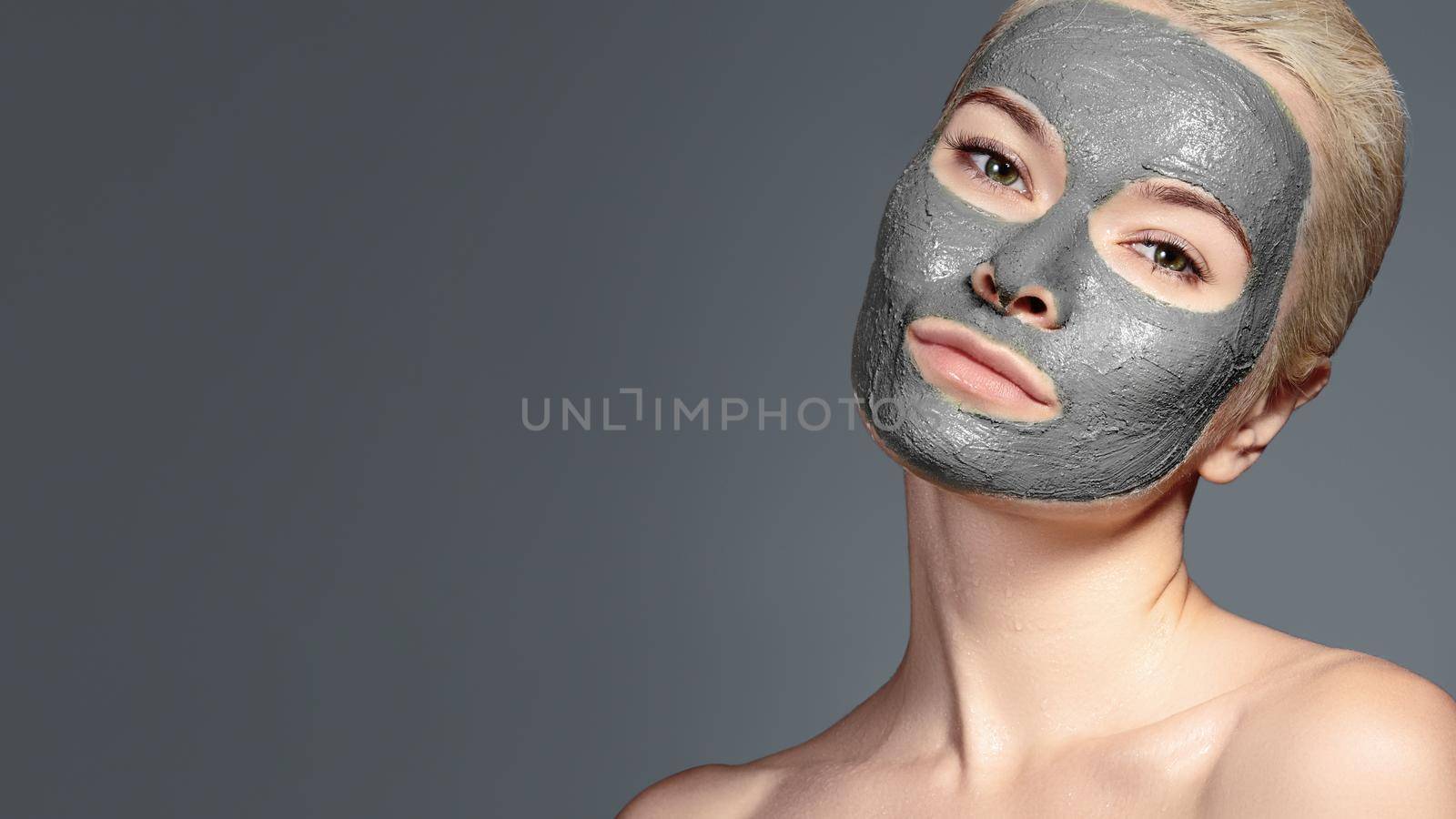 Beautiful Woman Applying Black Facial Mask. Beauty Treatments. Close-up Portrait of Spa Girl Apply Clay Facial mask on grey background.