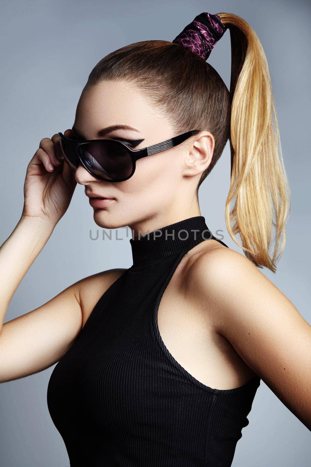 Beautiful young woman with black fashion sunglasses and glamour ponytail hairstyle on blue background. Trendy look for lady. Eye wear style.