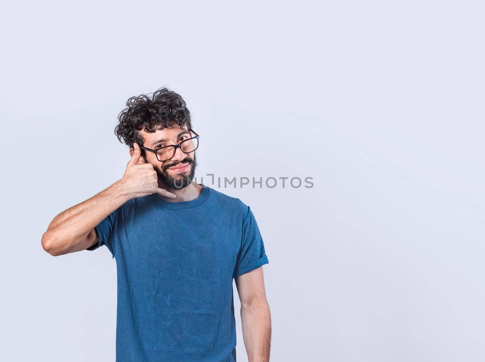 Attractive caucasian young male in casual clothes imitates telephone conversation, keeps hand near ear as if holding mobile phone