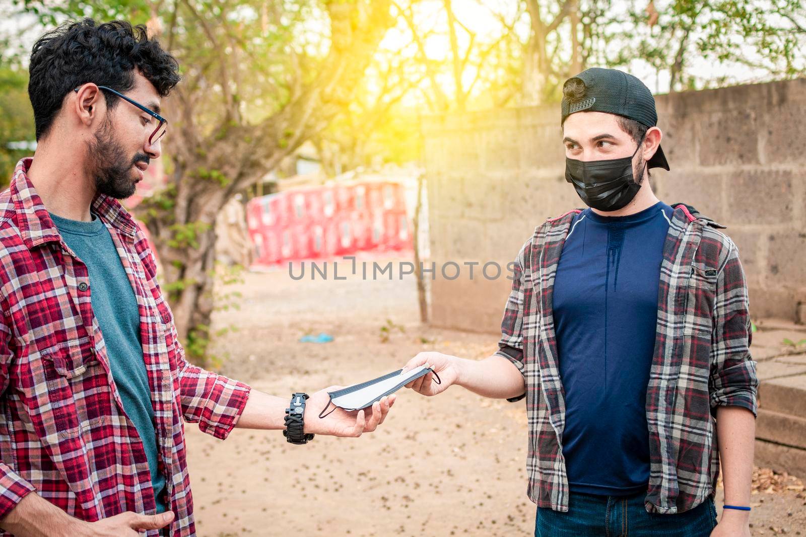 Two young people giving each other a mask, image of a young man giving a mask to another person, concept of a person offering a mask