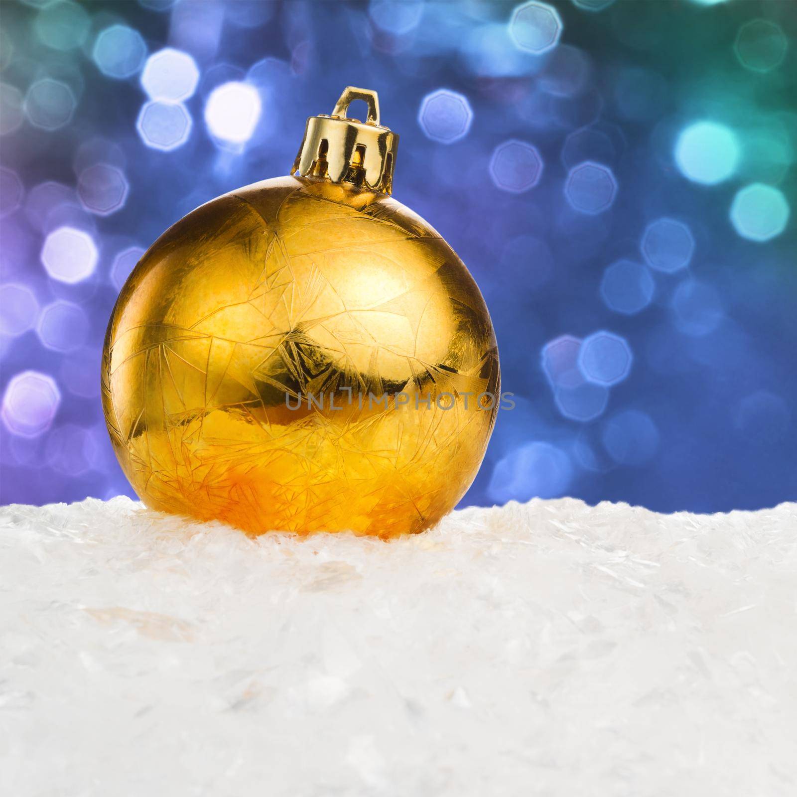 Golden Christmas ball on snow over blue festive background with copy space