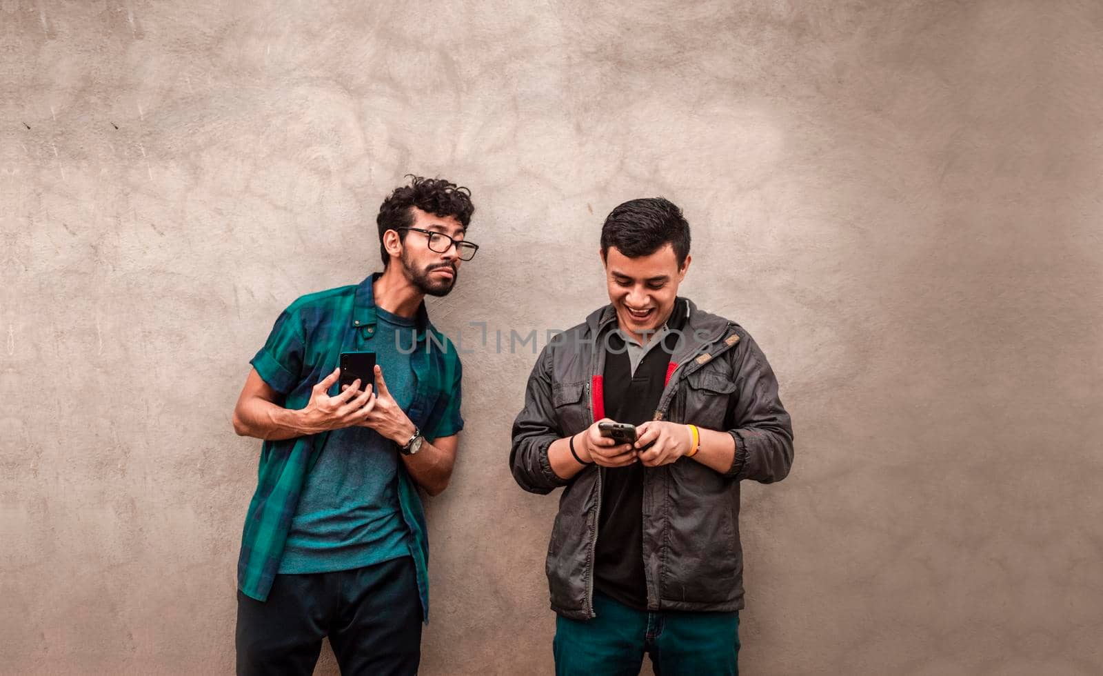 Young latin man spying on another cell phone, man showing his cell phone to another guy by isaiphoto