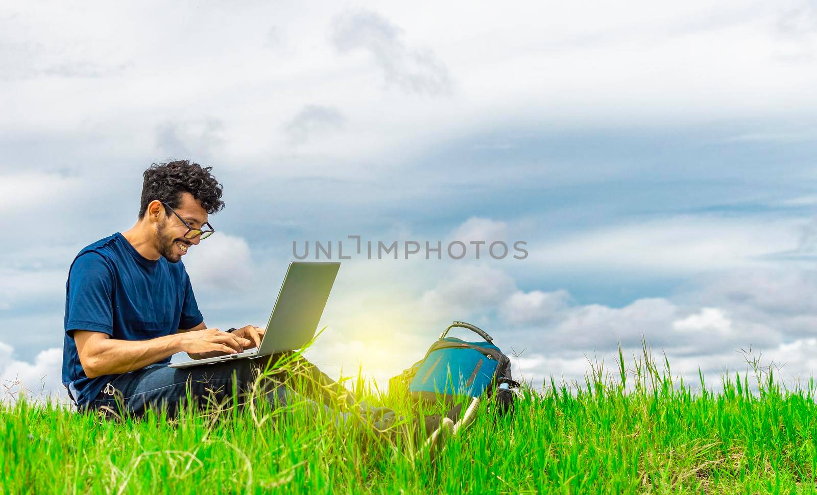 Young man in glasses working on his laptop, man in the field with his computer