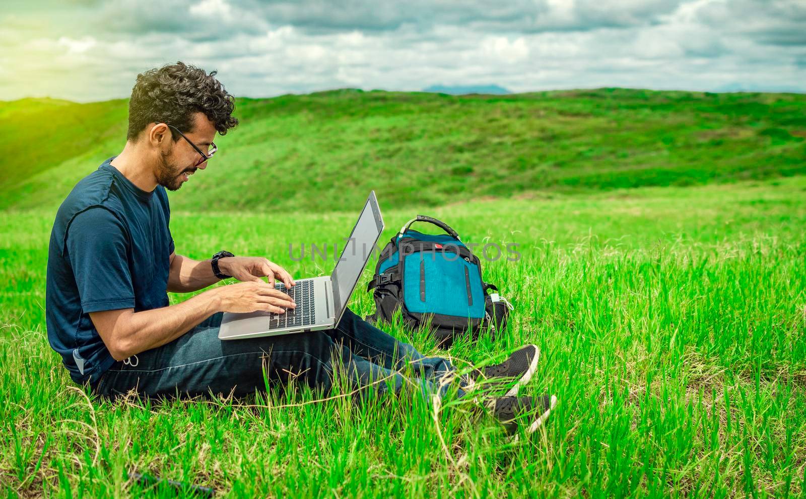 Young man in glasses working on his laptop, man in the field with his computer