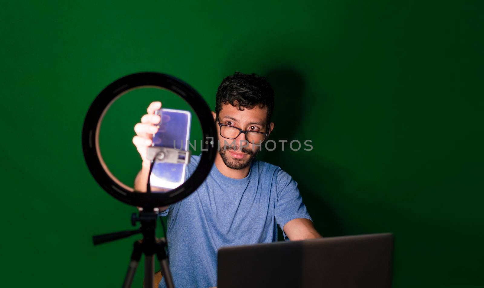 Young man with laptop making video blog, Young man creator contents with celphone, man with his laptop making video call with green background,