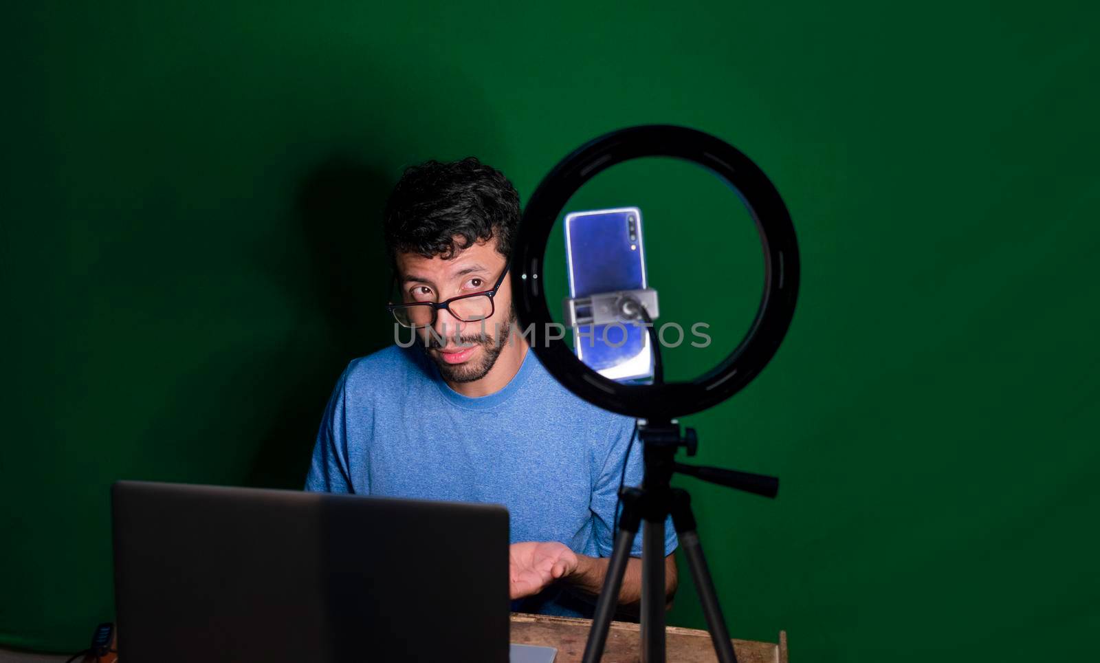 Young man with laptop making video blog, Young man creator contents with celphone, man with his laptop making video call with green background,