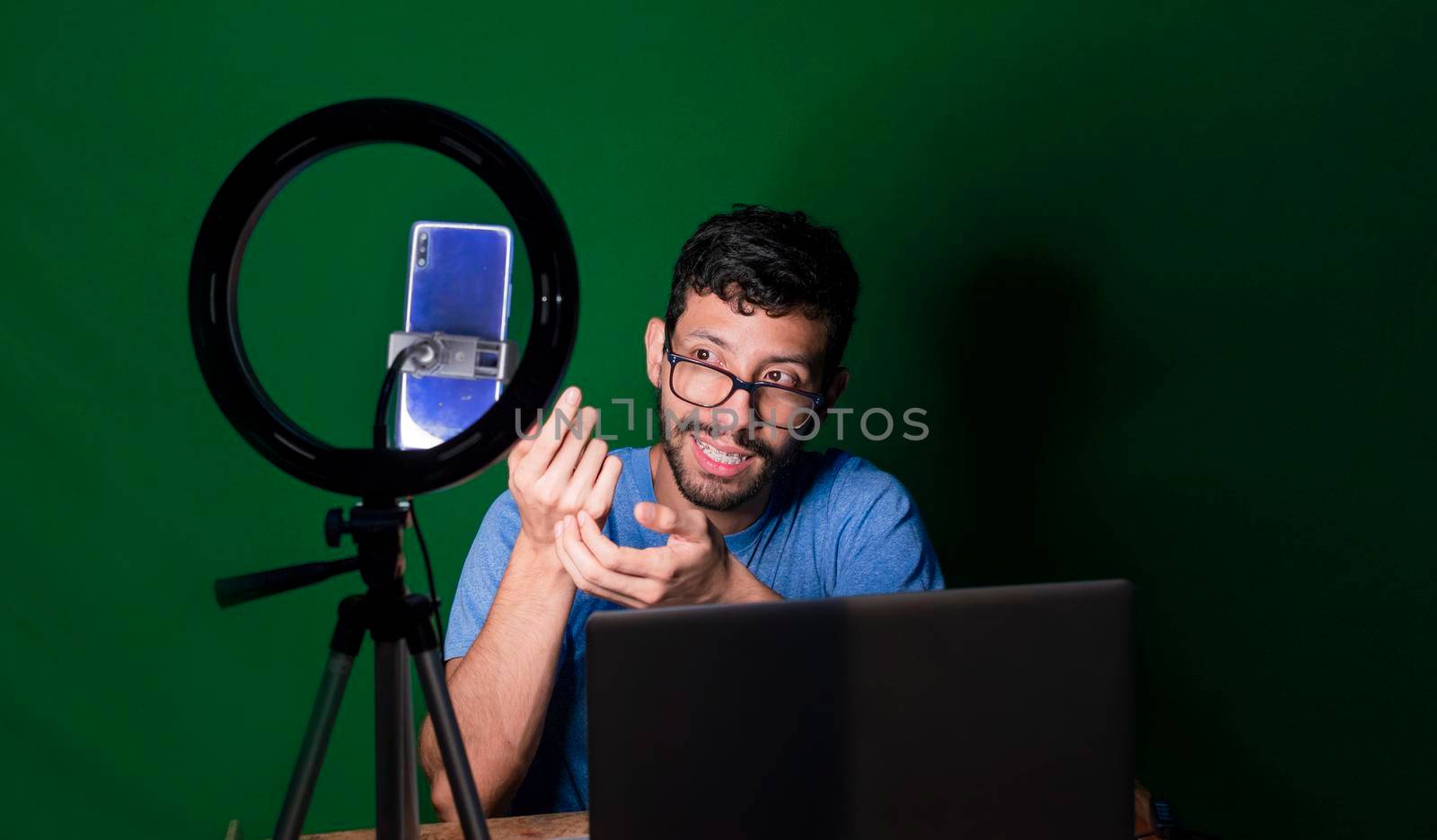 Young man with laptop making video blog, Young man creator contents with celphone, man with his laptop making video call with green background,