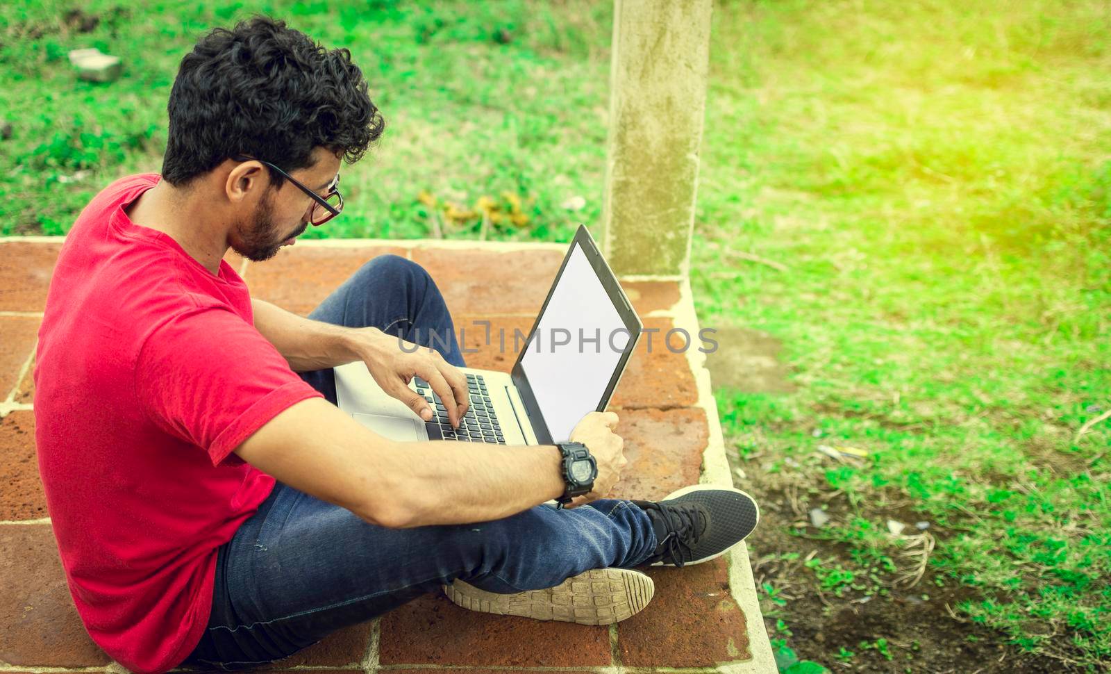 Young man in glasses working on his laptop, man on the floor with his computer