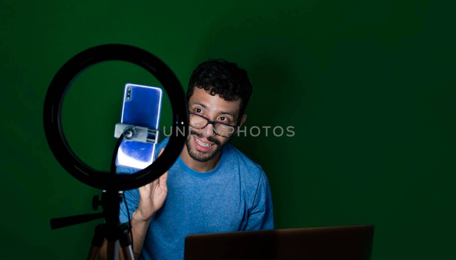 Young man with laptop making video blog, Young man creator contents with celphone, man with his laptop making video call with green background,