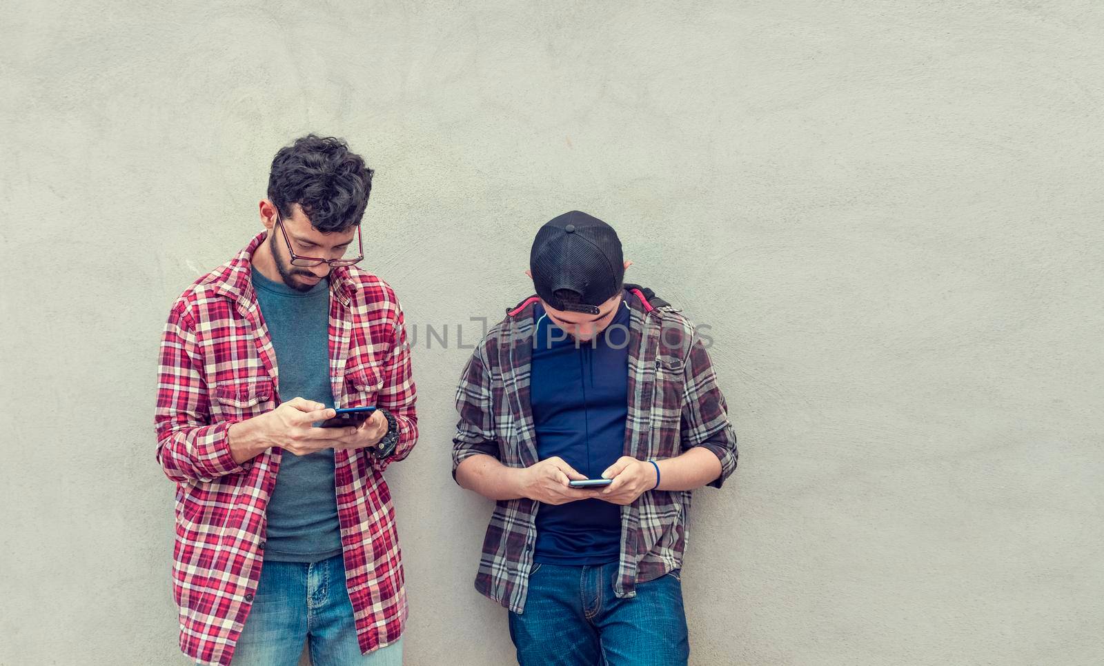 Two guys checking their cell phones, Smiling attractive young people checking their cell phones, Two guys with their cell phones by isaiphoto