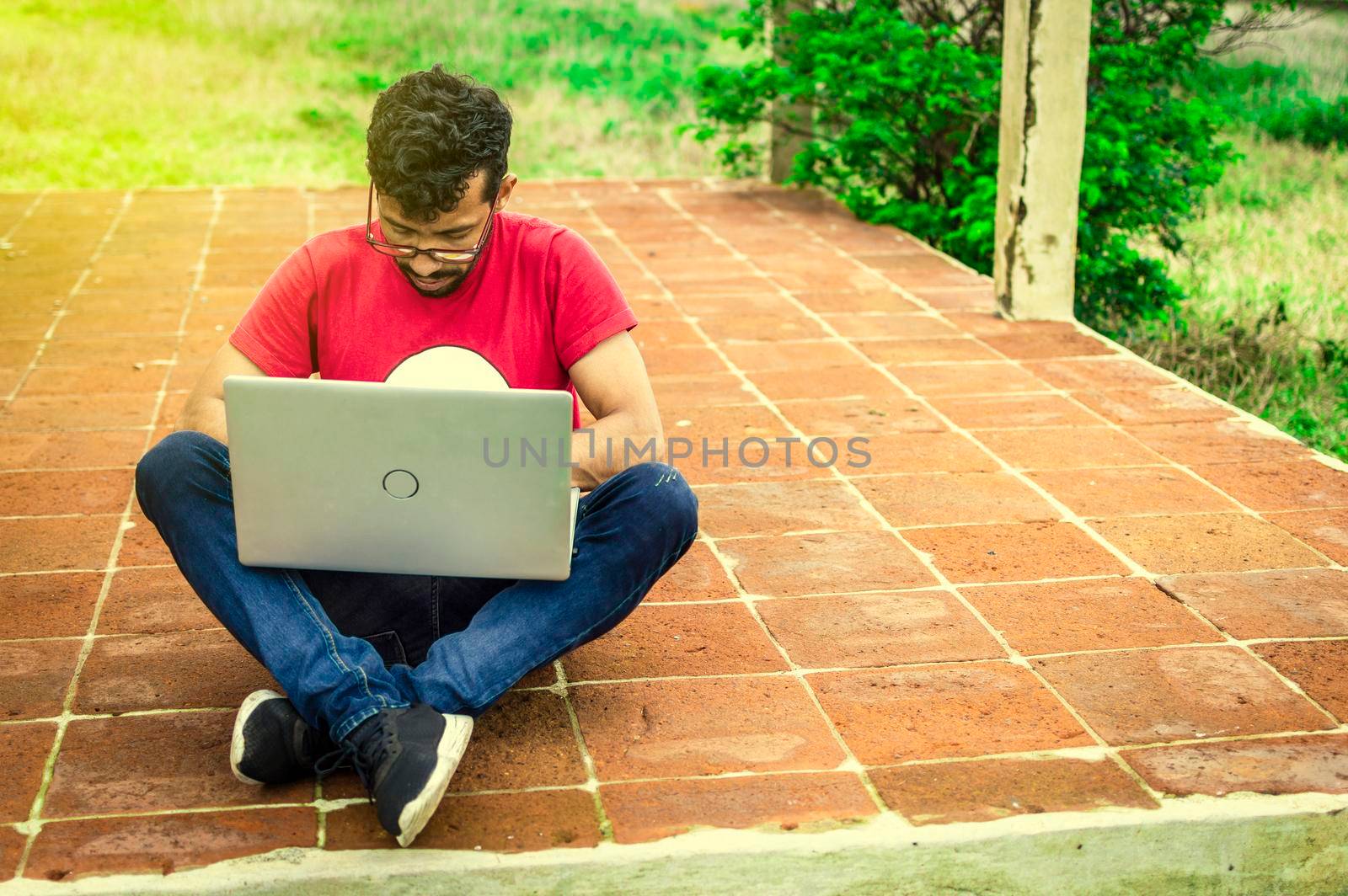 Young man in glasses working on his laptop, man on the floor with his computer