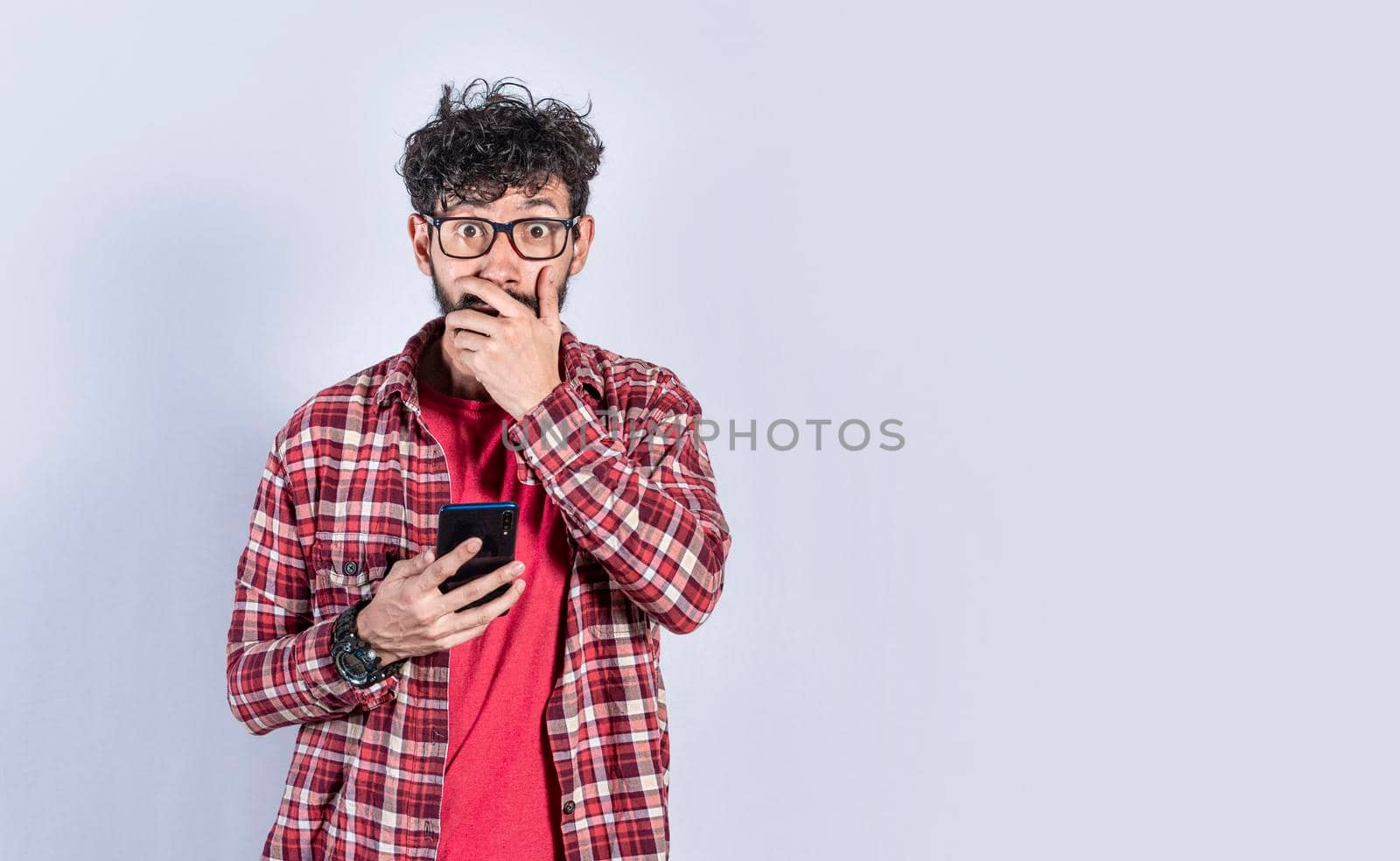 Young man with his cell phone covering his mouth, concept of a man stunned with his cell phone by isaiphoto