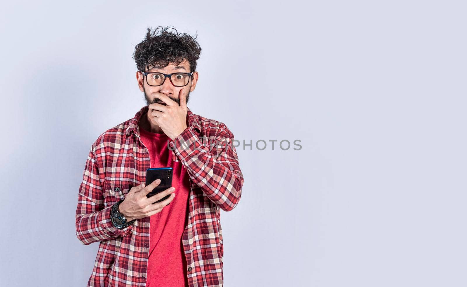 Young man with his cell phone covering his mouth, concept of a man stunned with his cell phone