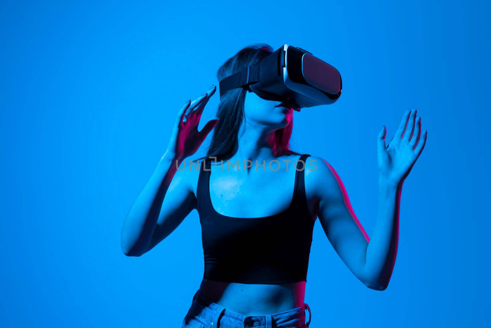 Young woman working in VR goggles on a grey background. Modern architect using virtual reality glasses at workplace. Designer working in augmented reality vr studio