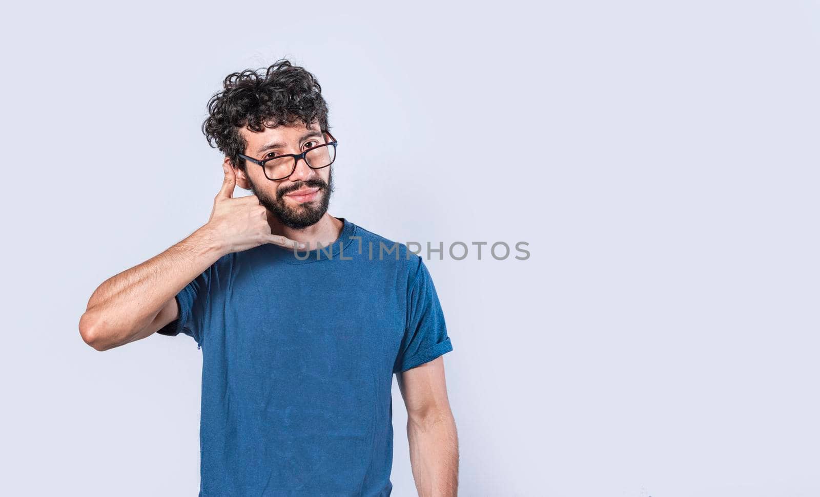 Attractive caucasian young male in casual clothes imitates telephone conversation, keeps hand near ear as if holding mobile phone