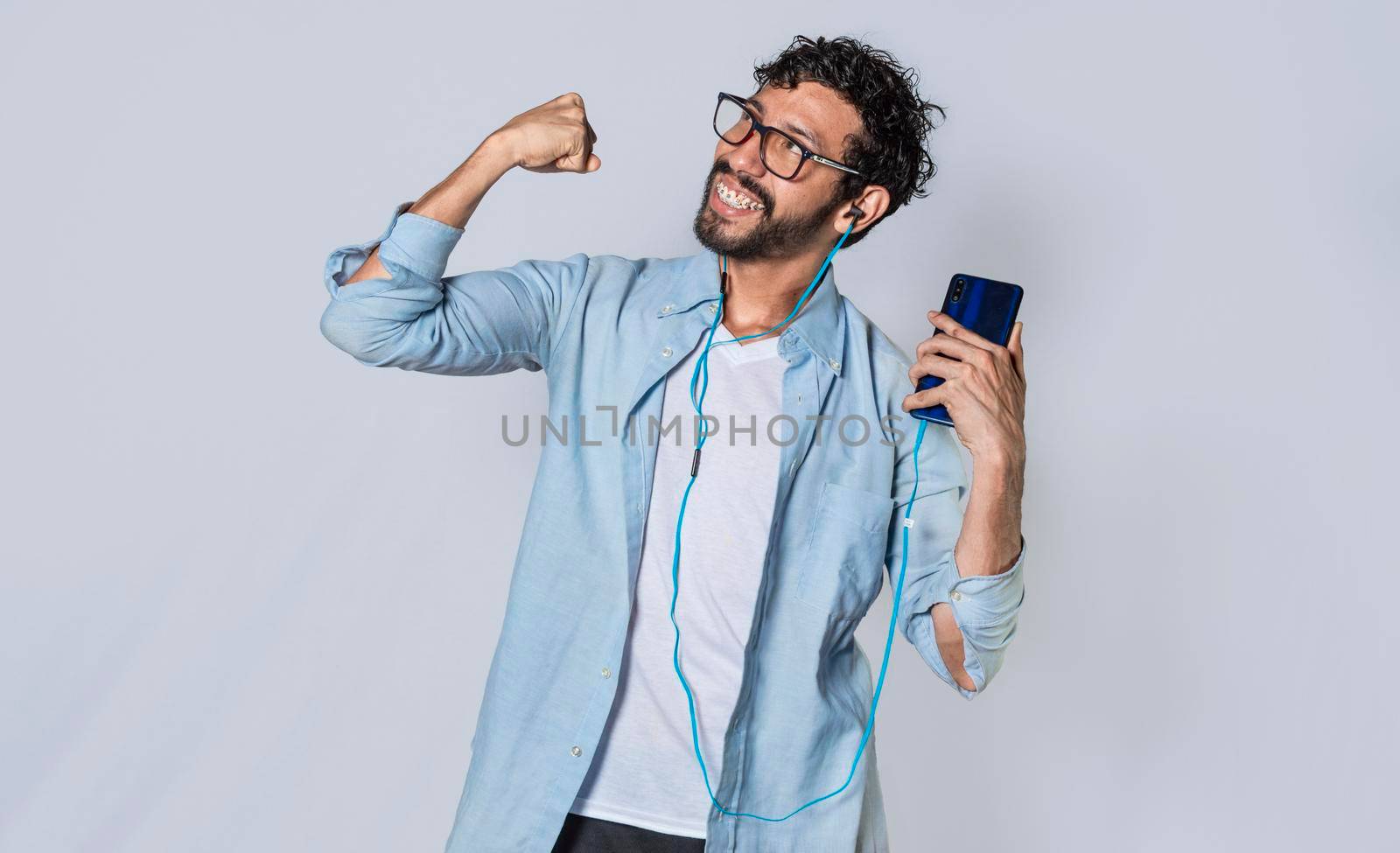Happy man with headphones holding a cell phone and celebrates, A guy with his smartphone celebrating victory by isaiphoto