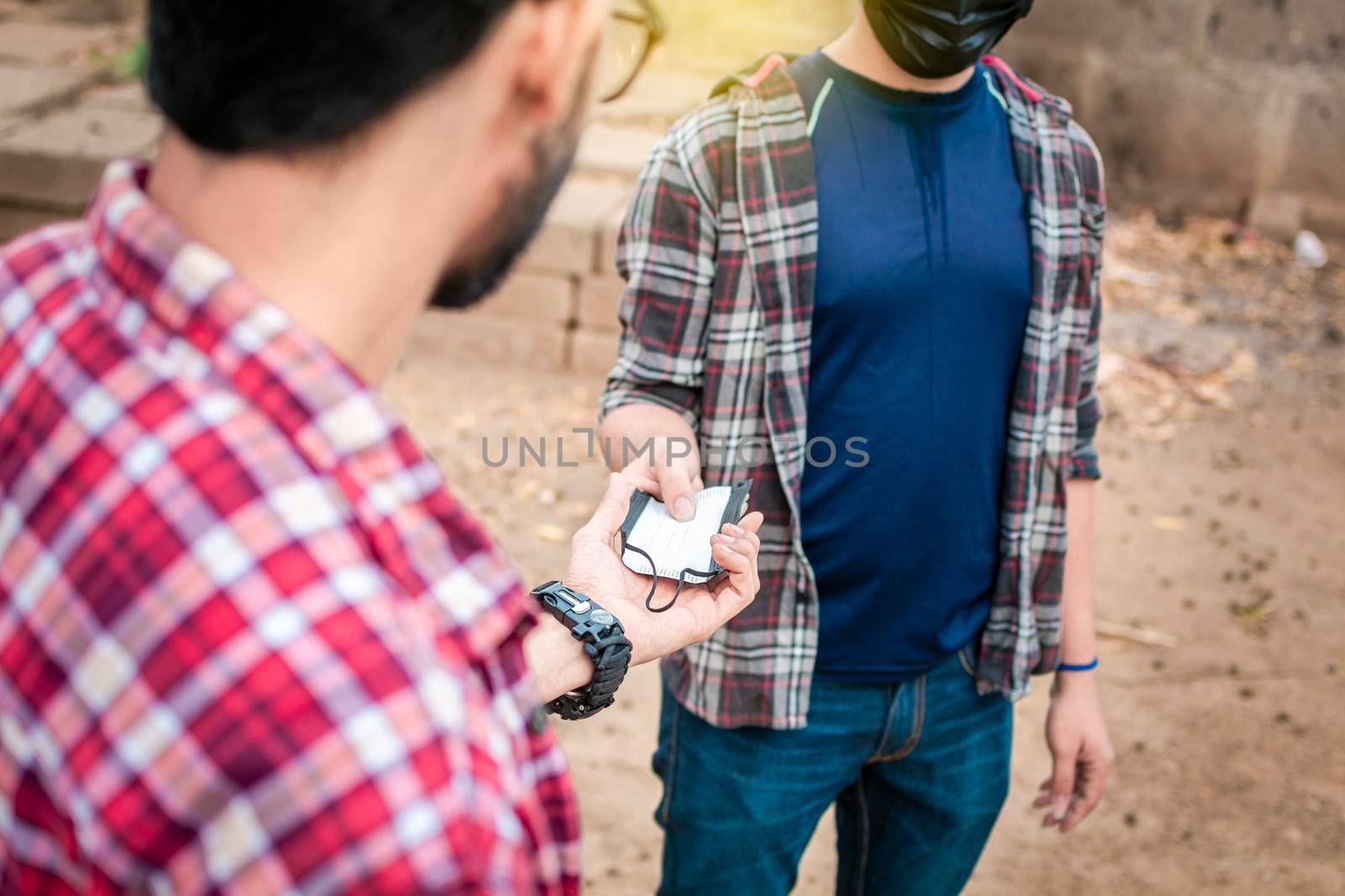 Two young people giving each other a mask, image of a young man giving a mask to another person, concept of a person offering a mask