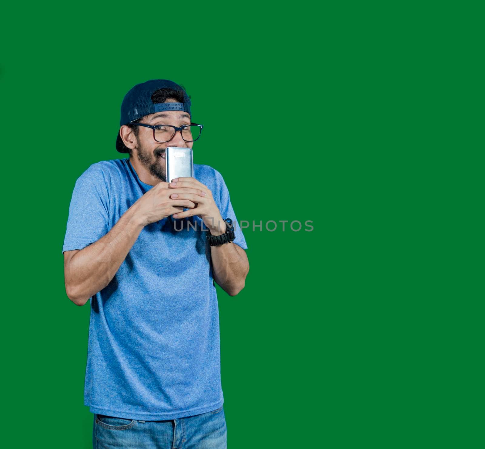 boy in glasses smiling with his cell phone, young man in cap smiling while holding his cell phone on white background, boy smiling covering his mouth with cell phone