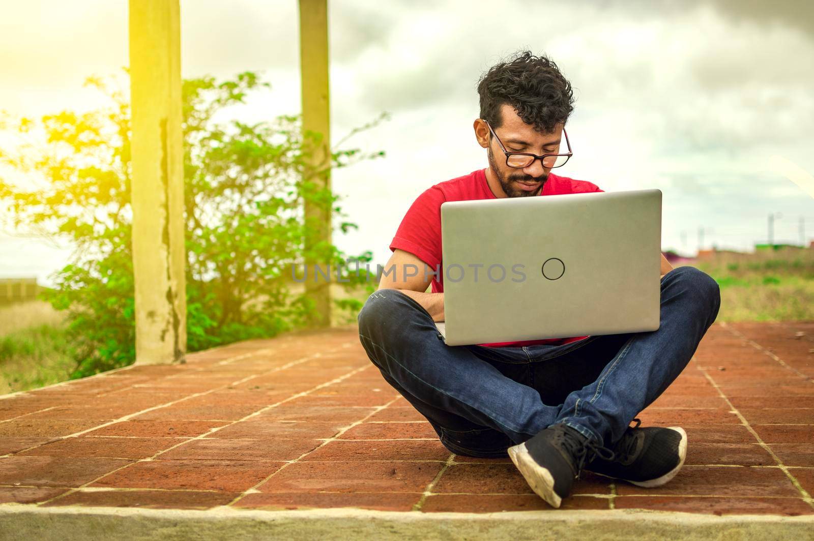 Young man in glasses working on his laptop, man on the floor with his computer
