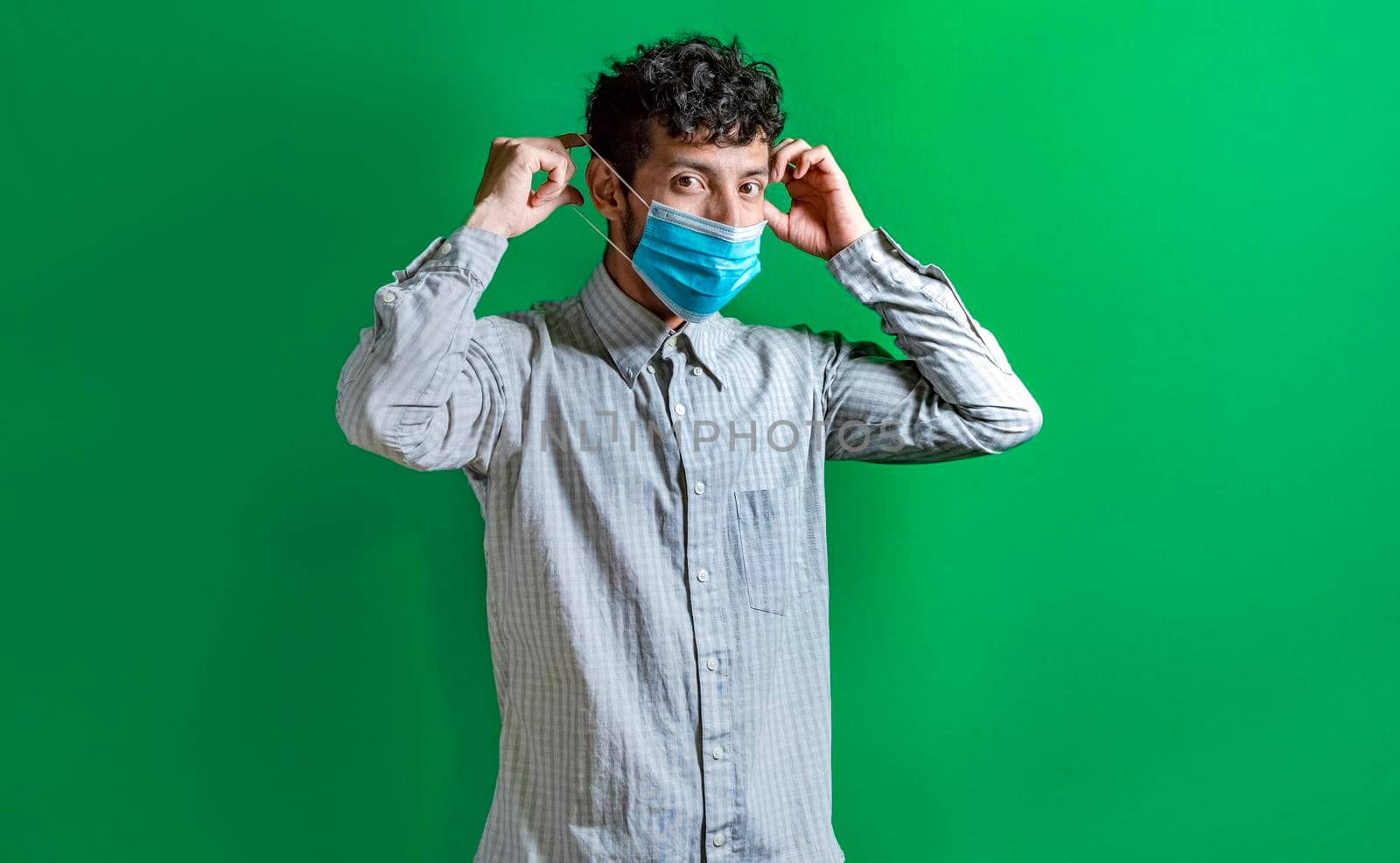 Young man putting on the mask on isolated background, concept of the correct use of the mask