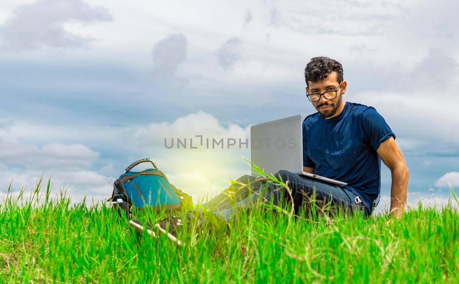 Young man in glasses working on his laptop, man in the field with his computer by isaiphoto