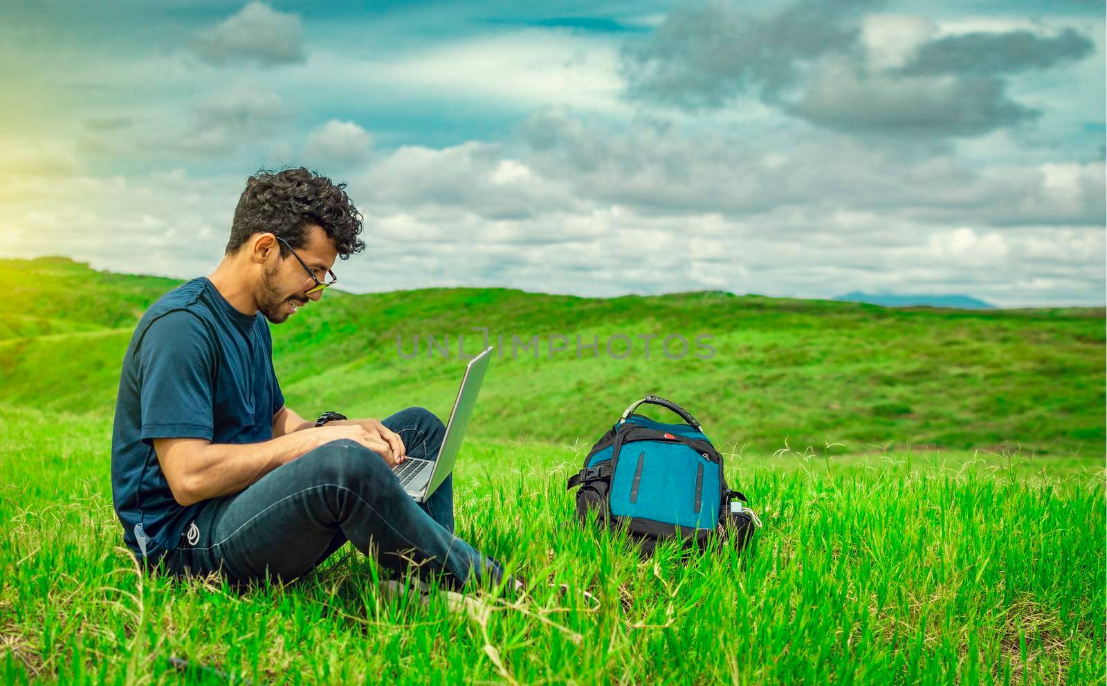 Young man in glasses working on his laptop, man in the field with his computer