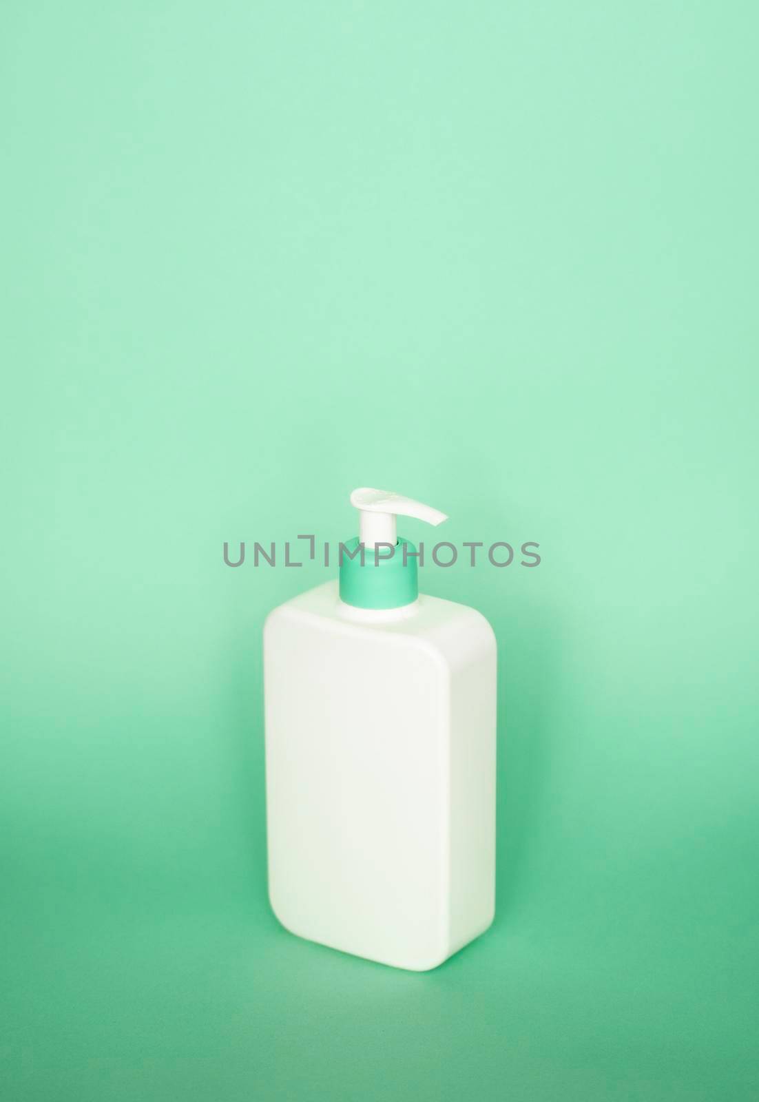 Large white plastic bottle with pump dispenser as a liquid container for gel, lotion, cream, shampoo, bath foam on green background