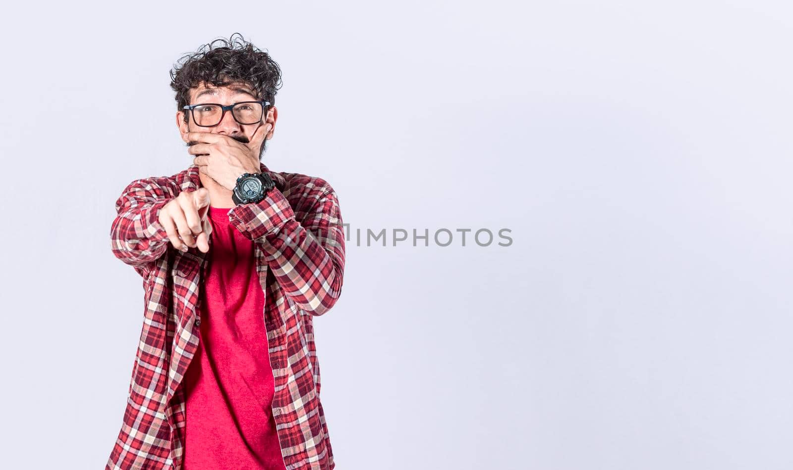 Isolated attractive guy laughing at you, young man pointing at camera with hand over mouth, male making fun of you