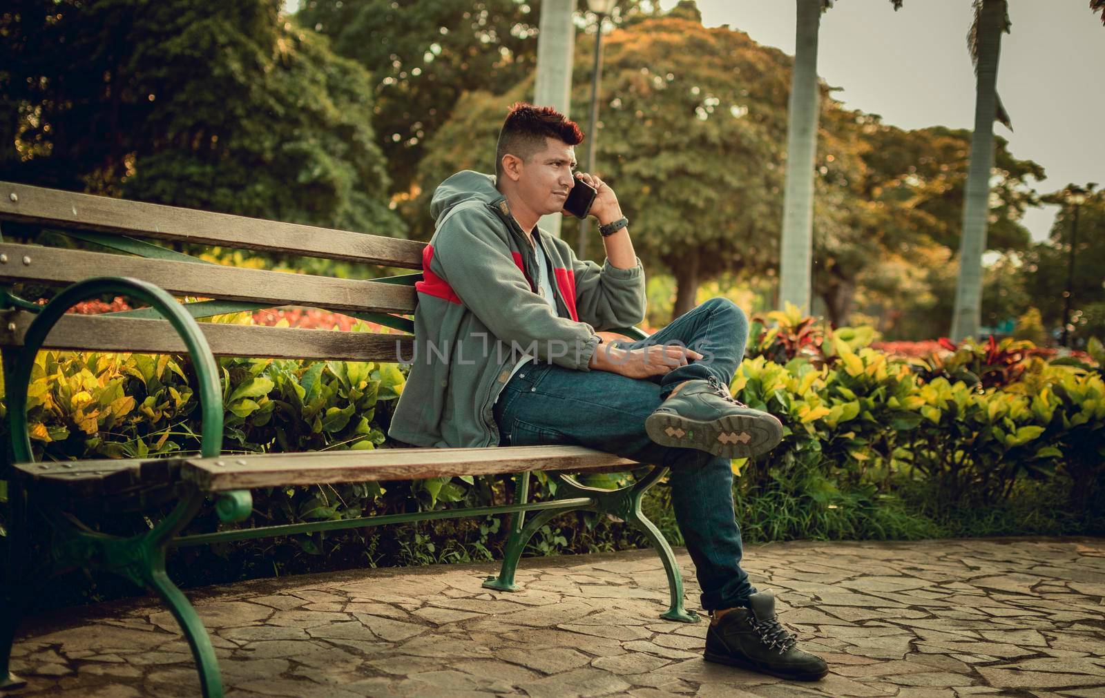 Man sitting on a bench calling on the phone, young man sitting on a bench with cell phone, close up of a young man calling on the phone sitting on a bench