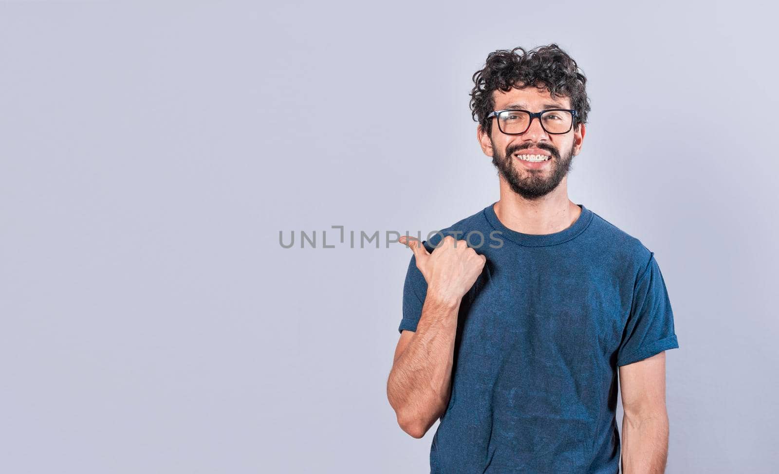 Cheerful bearded man with a friendly smile shows you the direction to a nice place, a friendly guy pointing his thumb to his right