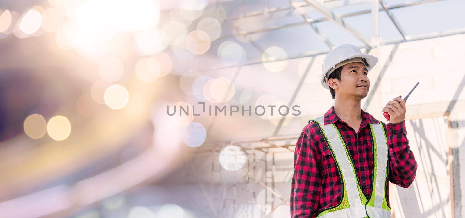 Asian engineer foreman architect worker man working at building construction site talking with radio by Sorapop