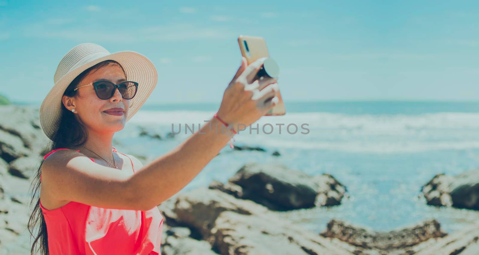 hat woman taking photos at sea, latin girl taking vacation photos, rear view of girl taking selfie on the beach