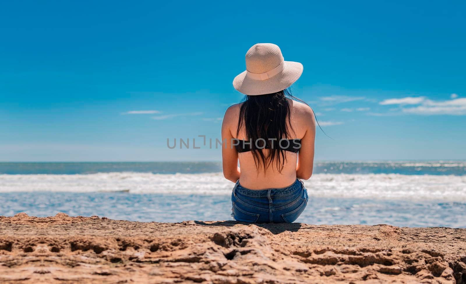 woman in hat from back to the sea, girl in hat looking to the sea, vacation concept, rear view of a girl watching the sea