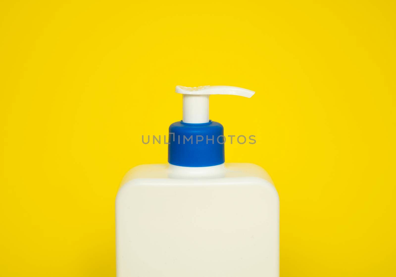 Large white plastic bottle with pump dispenser as a liquid container for gel, lotion, cream, shampoo, bath foam on yellow background