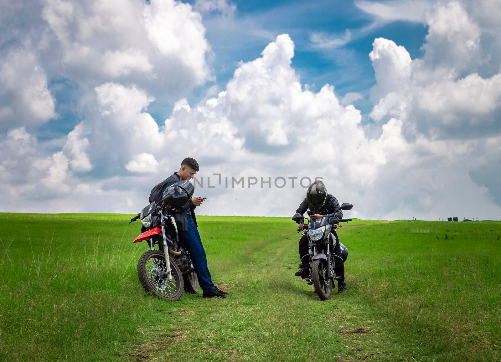 Two men with their motorcycles parked chatting in the field, two young motorcyclists in the field, two men on motorcycles on a beautiful country road, young motorcyclists parked on a road by isaiphoto